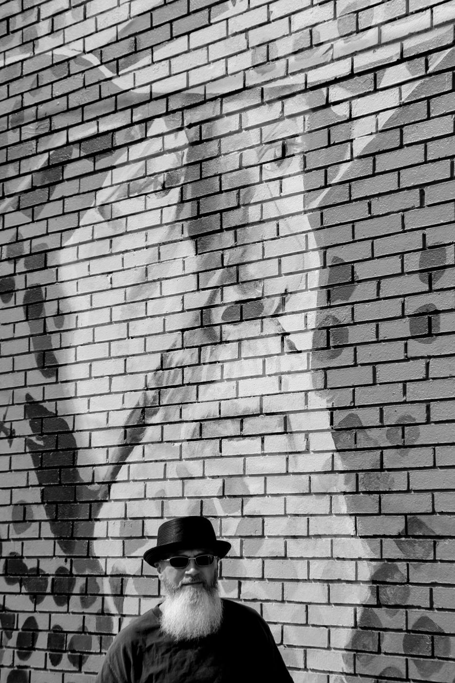 Mighty Rock in sunglasses against a wall, hands in pockets